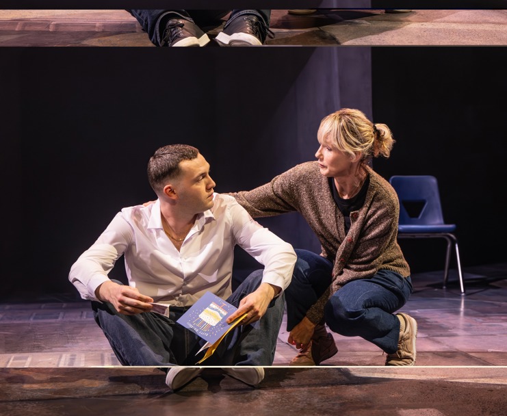 A young man in jeans and a white shirt sitting on the floor looking at a blonde woman seriously