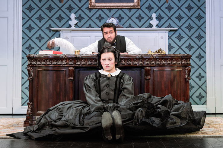 A performer dressed like President Lincoln sitting at a desk with a performer dressed in all black as Mary Todd Lincoln sitting on the floor pouting.