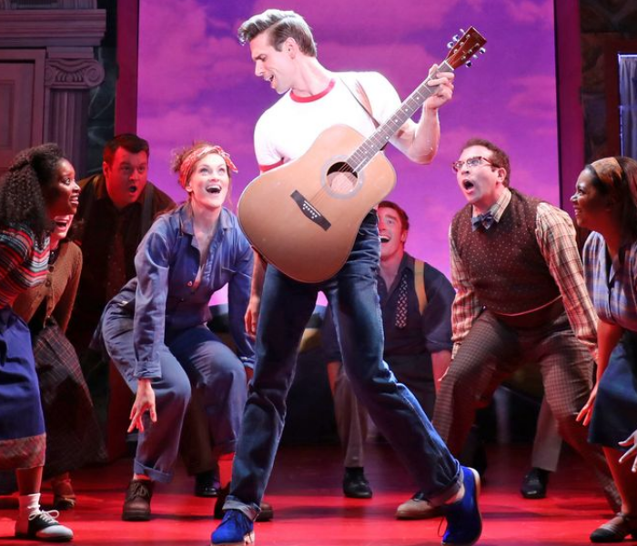 A man with a guitar posing like Elvis with young folks looking on in wonder