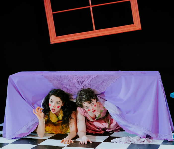 Two housewives with clown makeup under a dining room table 