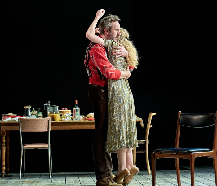 A man and a woman desperately embracing with a dining table in the background 