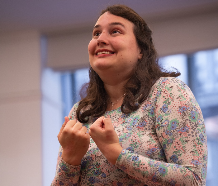 A woman with her fists balled and a strained grin