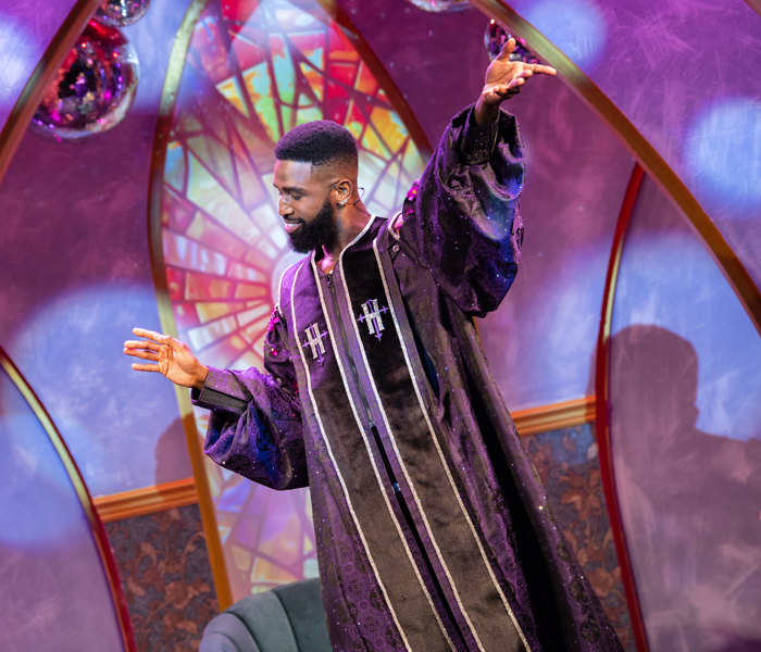 A man in priest robes preaching in front of a colorful background