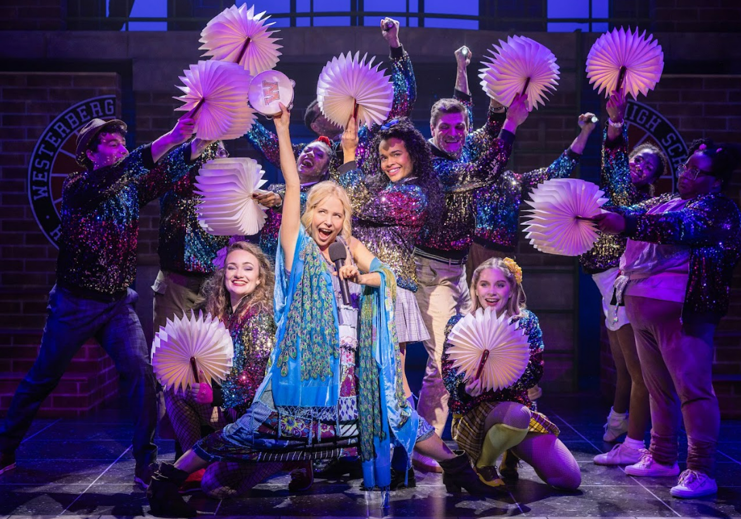 A blonde woman in blue singing with teens around her