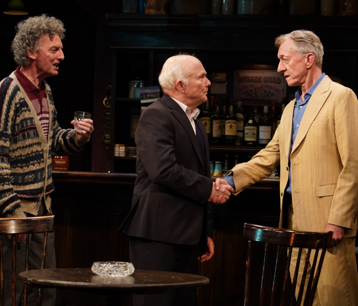 Three older men standing in a bar with two shaking hands